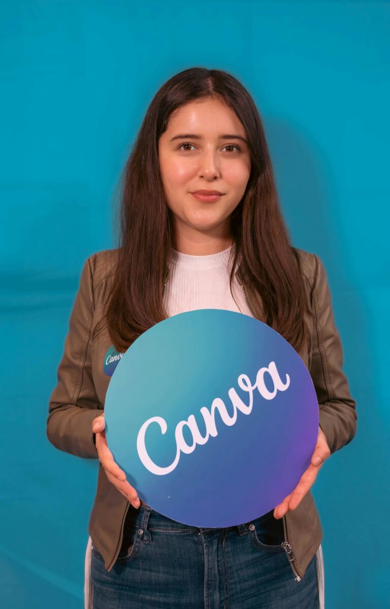 Portrait of a young woman holding a Canva logo sign, with a blue background.
